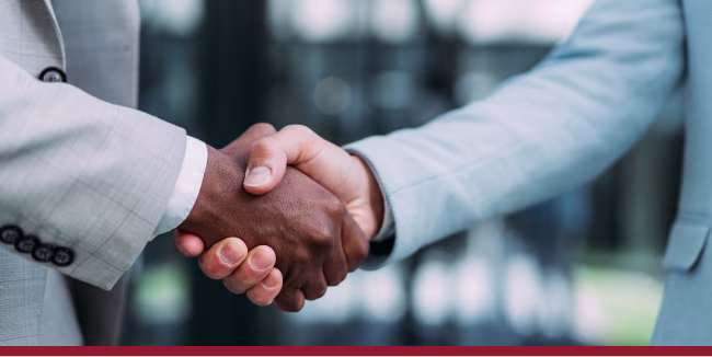 Close-up shot of two businessmen handshaking in front of modern office building. Focus is on the hands.