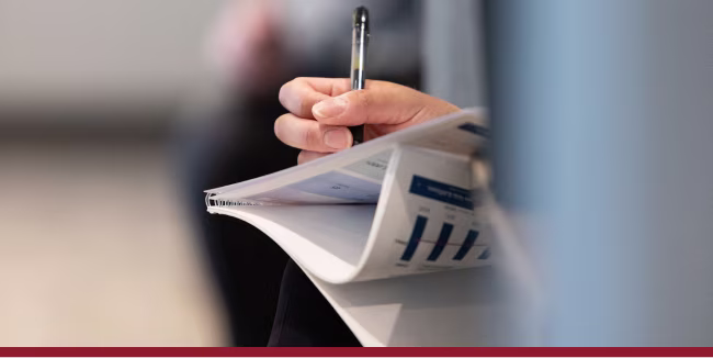 Person taking notes with a pen on a binded presentation deck.