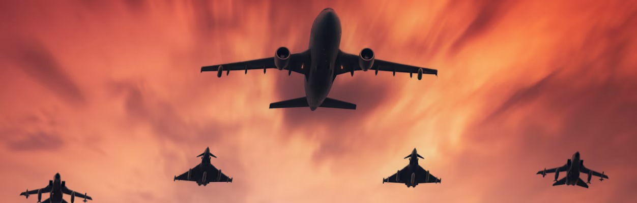 Military aircraft tanker in a convoy with fighter jets in the sky at sunset
