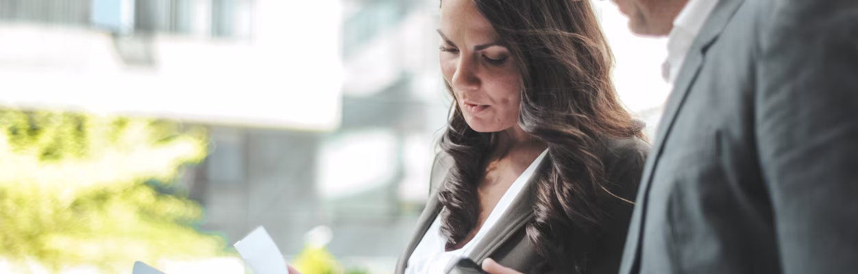 Two business professionals engaged in a serious discussion while reviewing documents and using a smartphone in an outdoor urban setting.