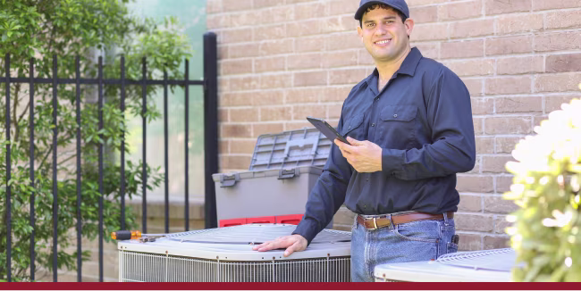 Blue collar air conditioner repairman working at residential home. He prepares to begin work by gathering appropriate tools and referring to digital tablet.