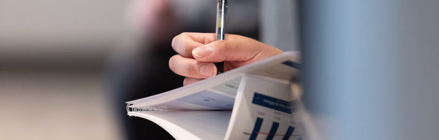 Person taking notes with a pen on a binded presentation deck.