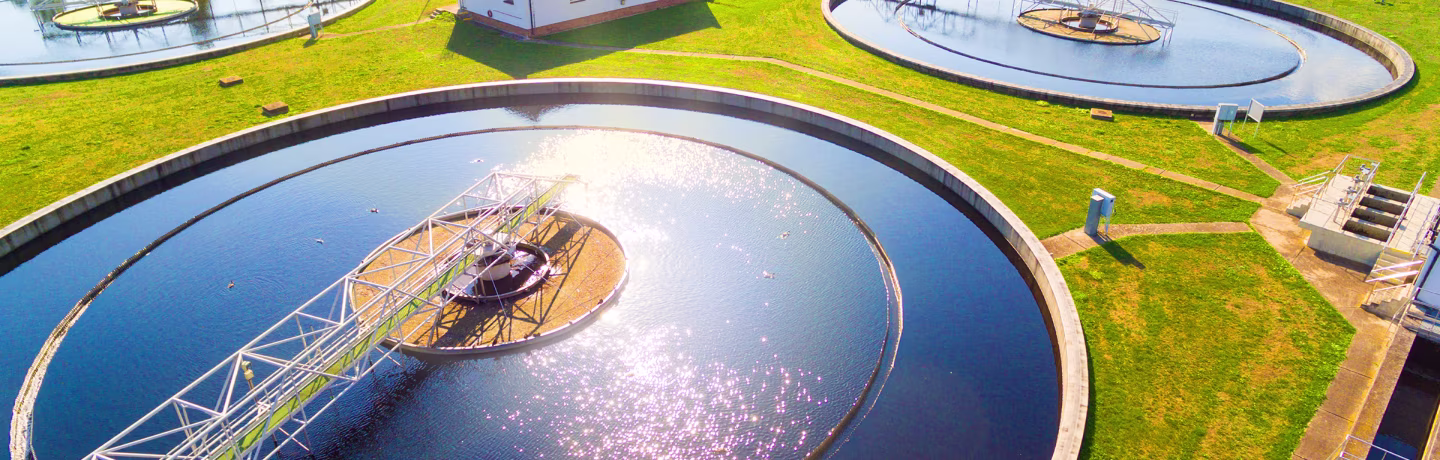 A circular wastewater reservoir with grass and buildings