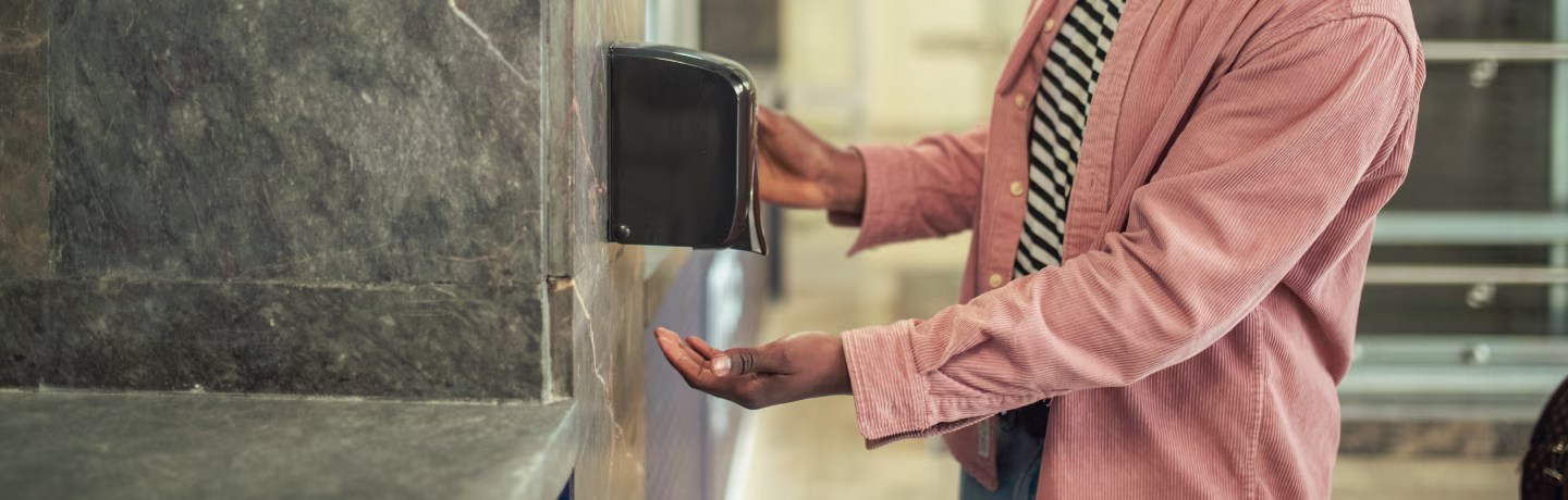 An African American man uses hand sanitizer while waiting for a bus at a station.