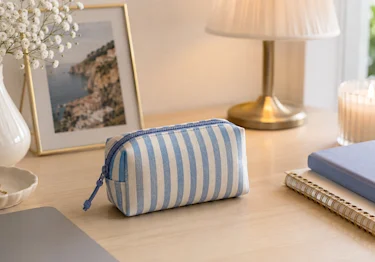 Blue striped zippered pouch on a desk for storing tampons and preventing wrapper ink transfer in a bag