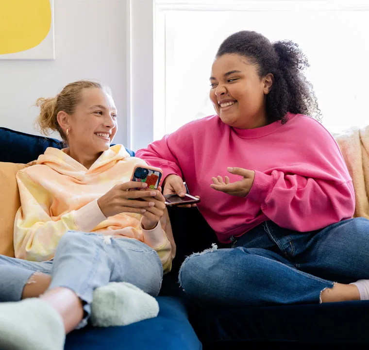 Two women face each other while comfortably lounging on a couch.