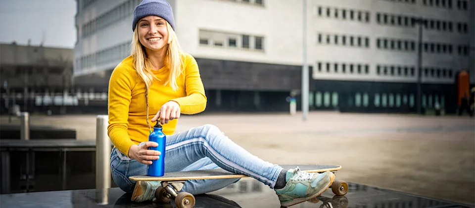 Young blonde girl drinking from a water bottle while sitting beside a skateboard