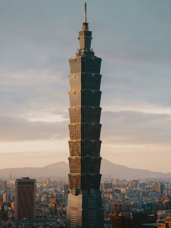 Taipei 101 skyscraper towering over the city skyline at sunset, with mountains in the background and golden light on its facade.
