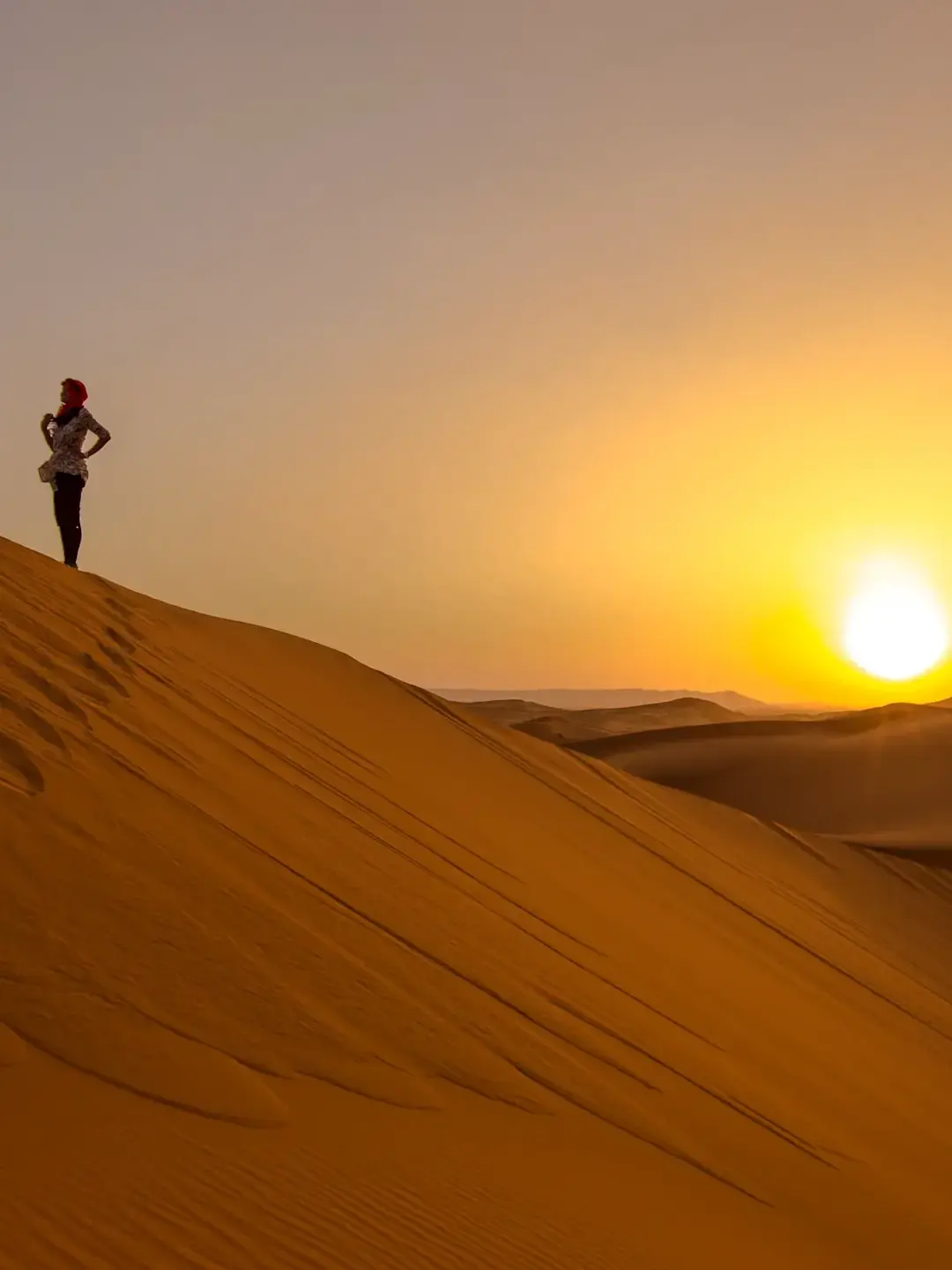 Silhouette of person standing on golden sand dune against vibrant sunset in desert landscape.