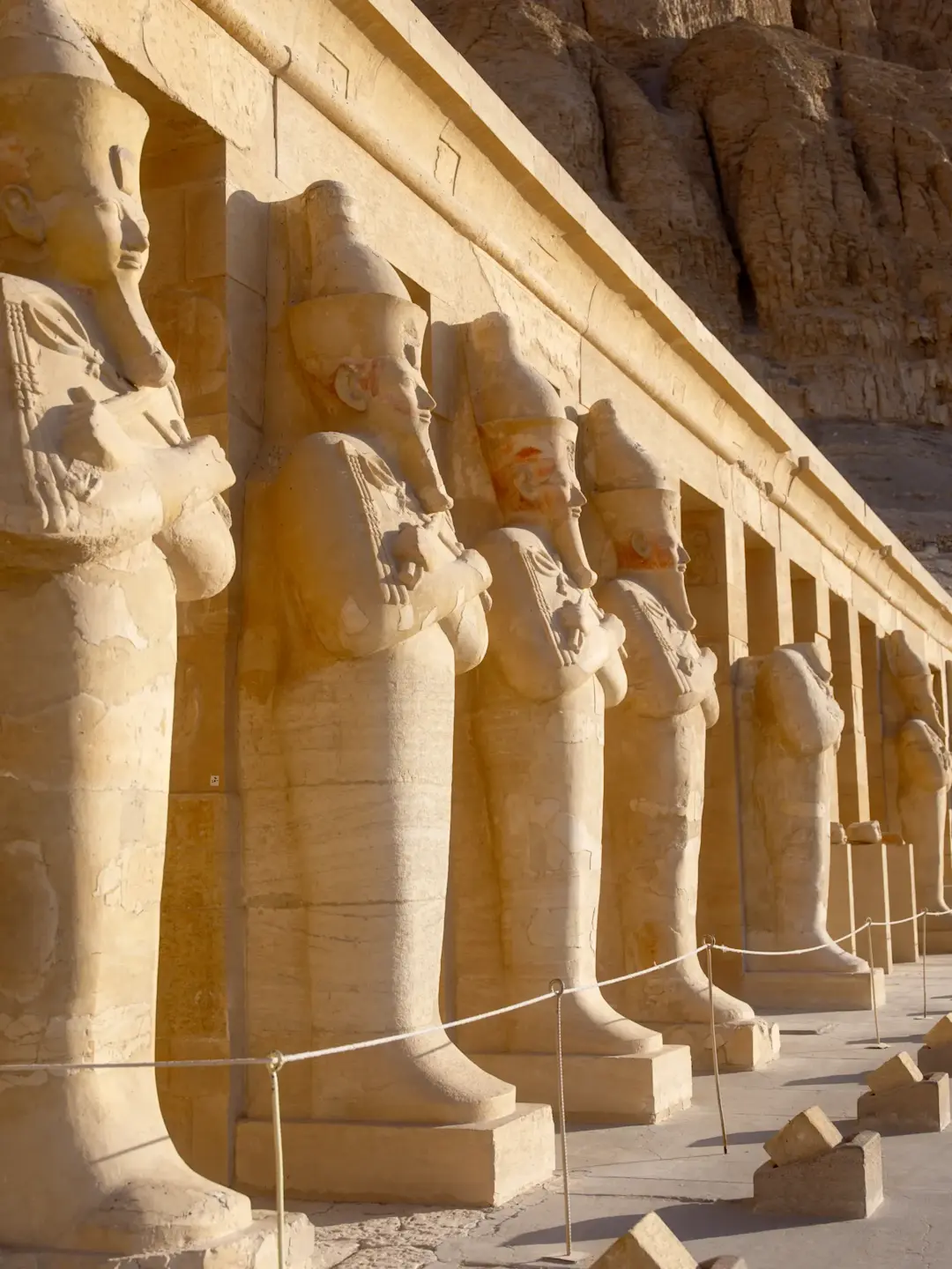 Ancient Egyptian statues at Hatshepsut's Temple, showing a row of sandstone figures with crowns and ceremonial dress.