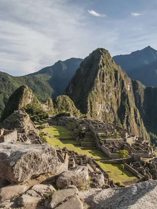 Ancient ruins of Machu Picchu nestled among green mountains under a cloudy sky in Peru.