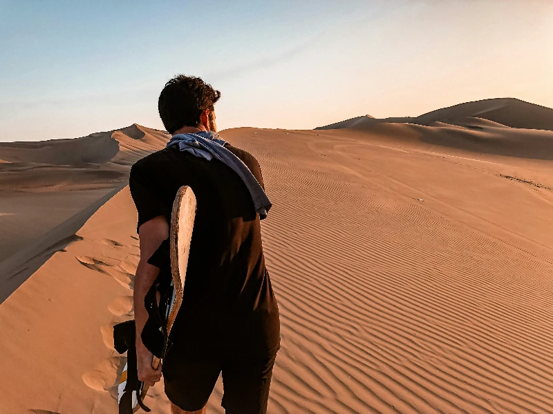 Person with scarf looking across vast golden sand dunes under clear blue sky at sunset.