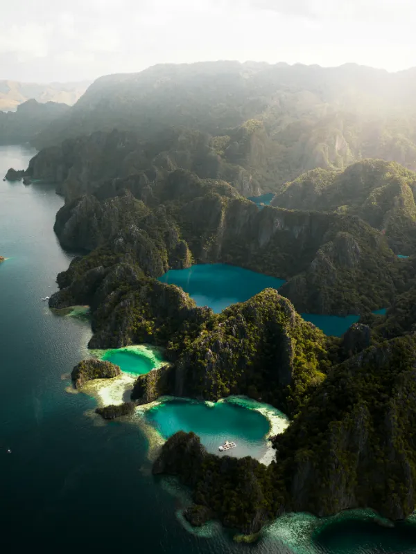 Aerial view of limestone islands with turquoise lagoons nestled between lush green cliffs, bathed in misty sunlight.