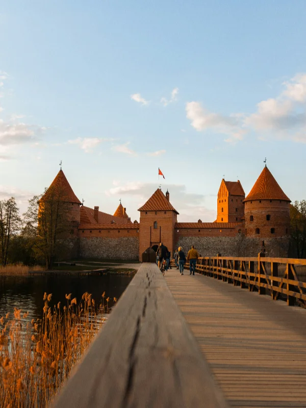 Wooden bridge leading to Trakai Island Castle with red brick towers and walls glowing in sunset light under a clear blue sky.