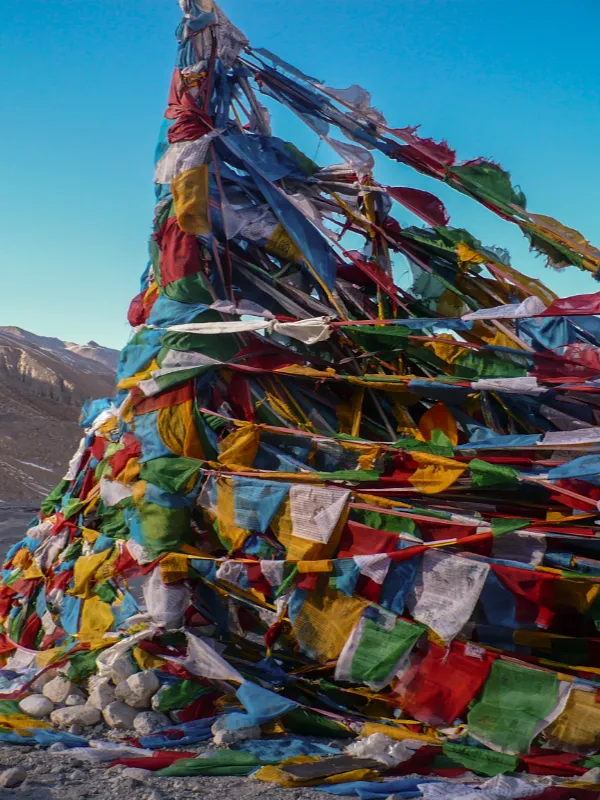 Colorful Tibetan prayer flags fluttering in the wind on a mountain structure against a clear blue sky.