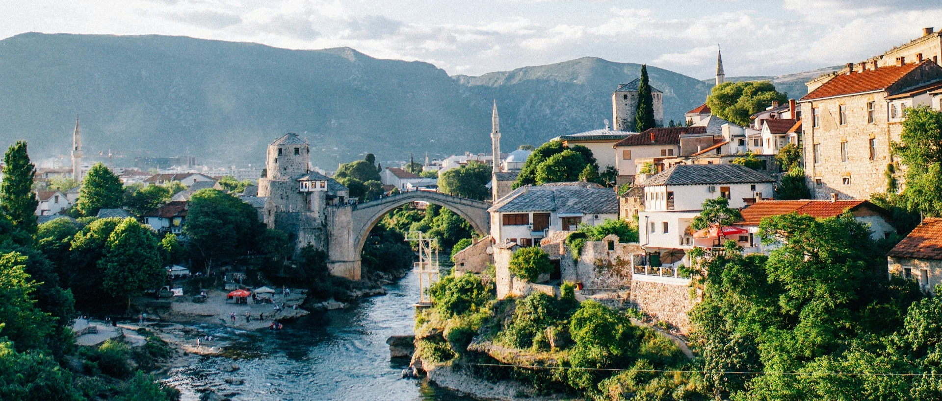Historic Mostar with its famous stone bridge spanning a blue river, surrounded by traditional buildings and mountains in the background.