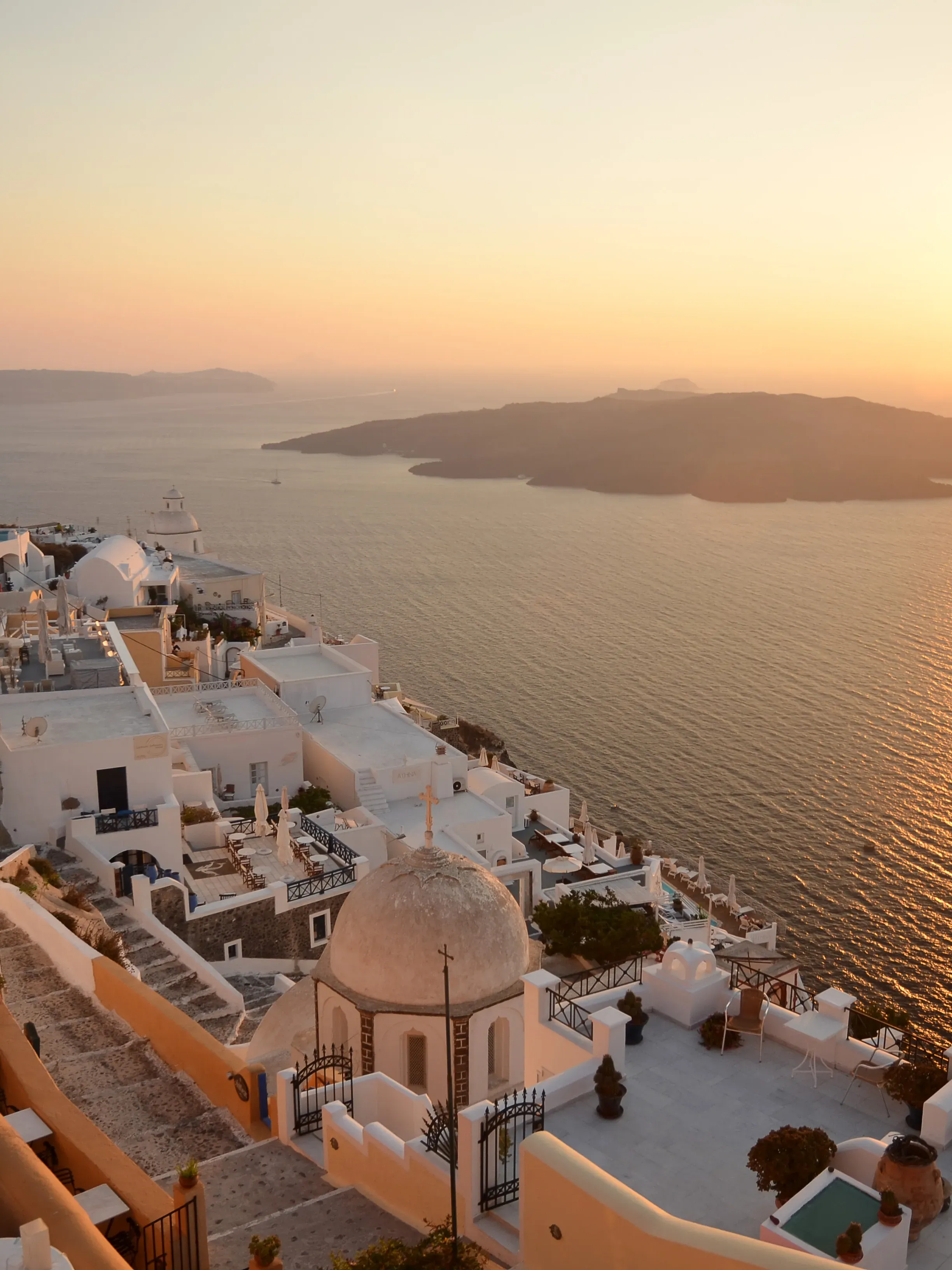 Sunset view of Santorini with white buildings cascading down the cliff, overlooking the Aegean Sea and volcanic caldera.