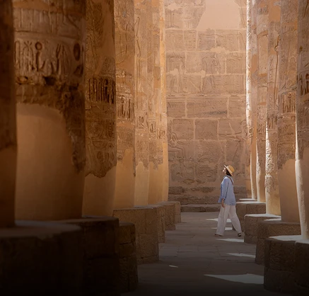 Person walking Egyptian temple with massive stone columns and hieroglyphics carved on walls