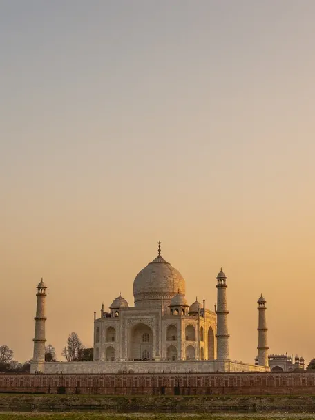 The Taj Mahal illuminated by golden sunset light, its white marble dome and minarets standing majestically against a warm orange sky.