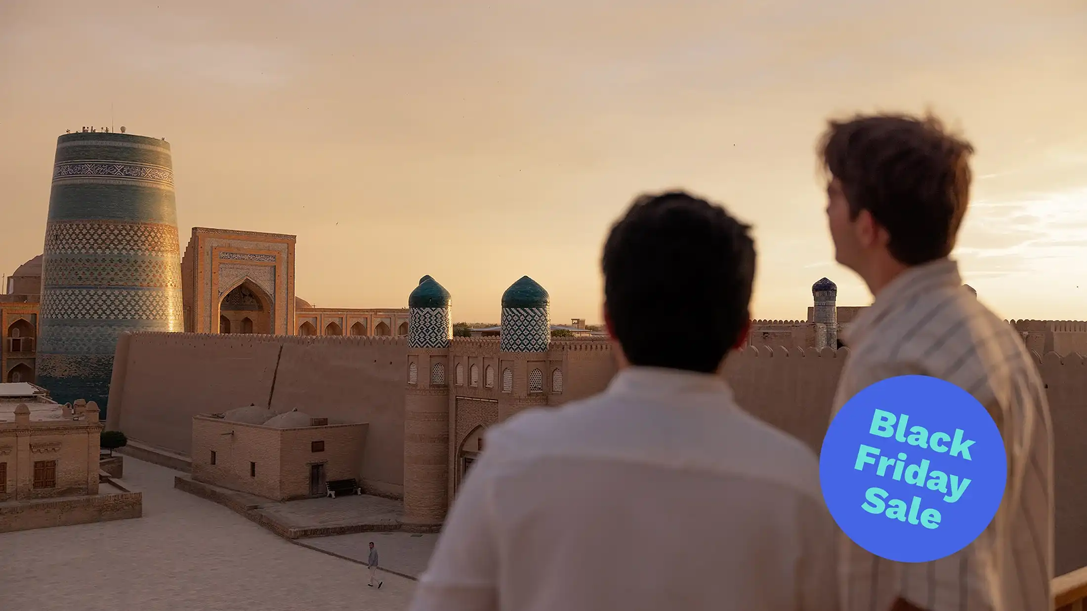 Two people overlook an ancient Central Asian city at sunset, with a tiled minaret and mosque. A Blue Friday Sale badge is visible.
