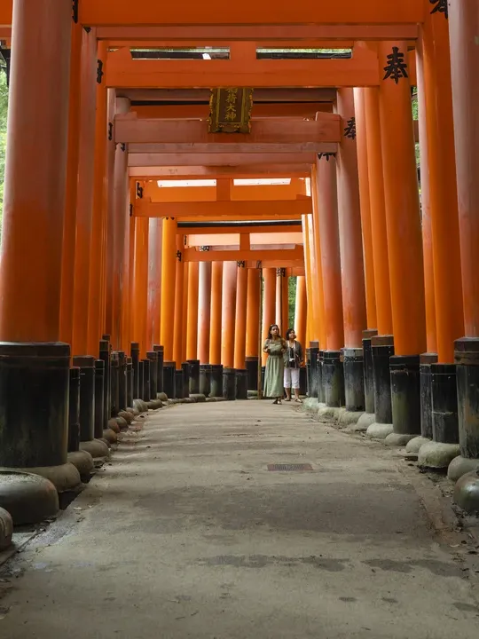 Pathway through vibrant orange torii gates at a Japanese shrine with visitors walking in the distance.