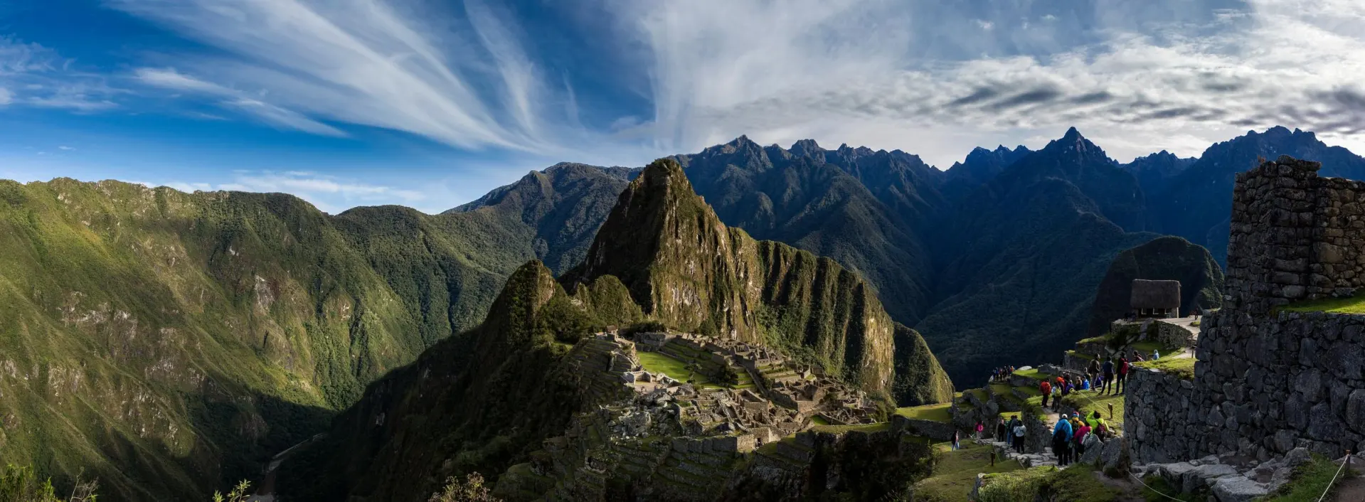Panoramic view of Machu Picchu, the ancient Incan citadel nestled among green mountains under dramatic blue skies with wispy clouds.