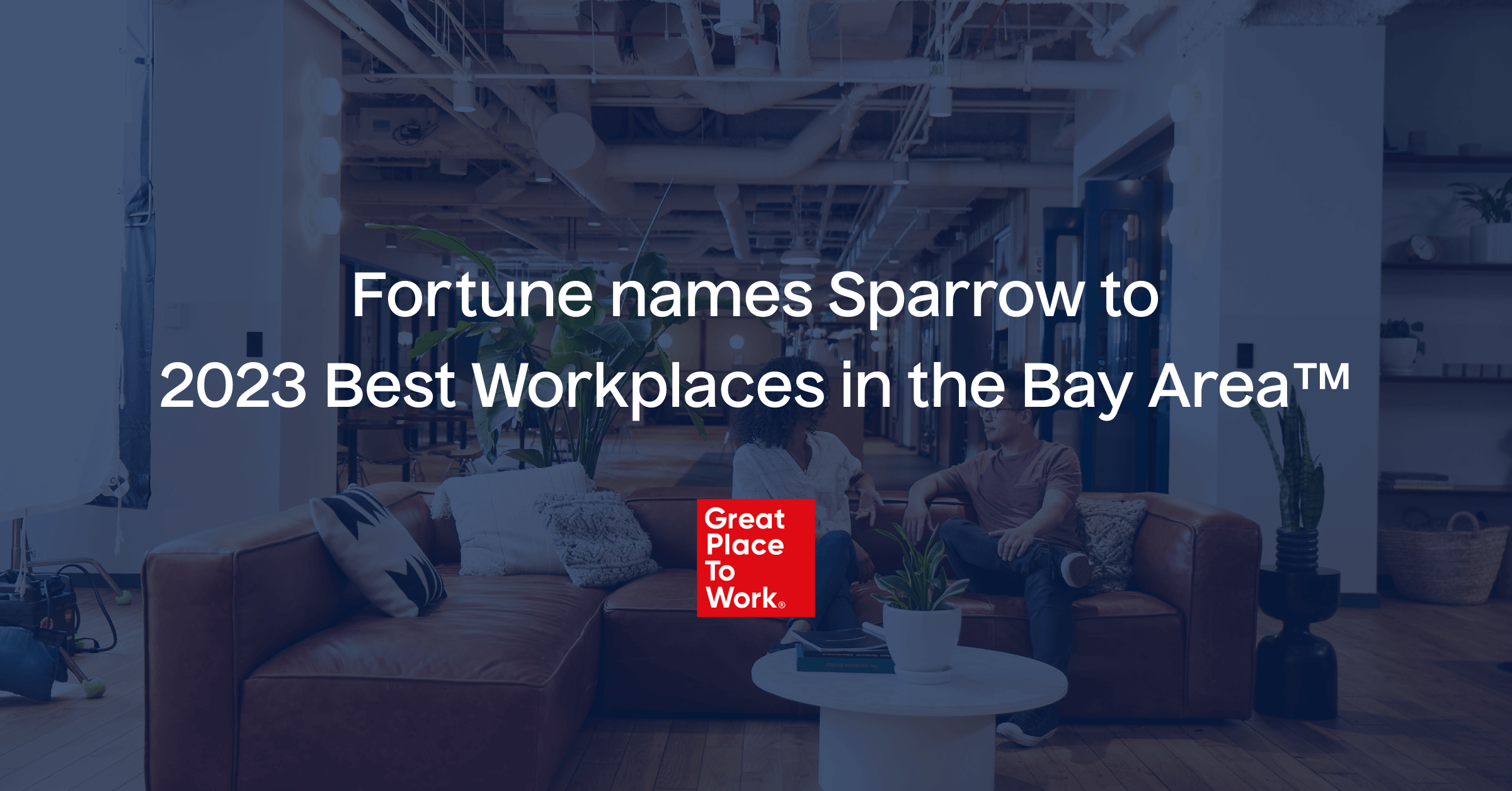 A cozy office lounge area with a modern design, featuring a sofa, throw pillows, and a coffee table with books and a potted plant. Text overlay reads, "Fortune names Sparrow to 2023 Best Workplaces in the Bay Area™" with a "Great Place To Work" logo below. Employee experience is top-notch at Sparrow.