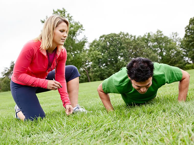 Lady helping a client with a personal training exercise in a park.