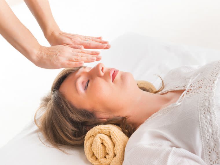 Practitioner providing Reiki treatment to a woman lying down.