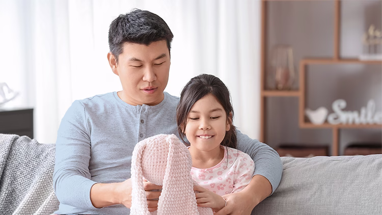 Parent and child sitting together on a couch, looking down at something, in a bright, cozy living room.