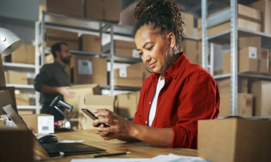 Woman working in warehouse on computer and smartphone