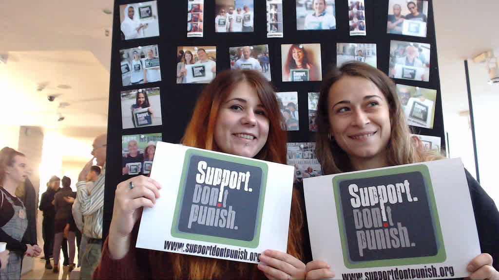 Two women holding up signs with the Support Don't Punish logo on them