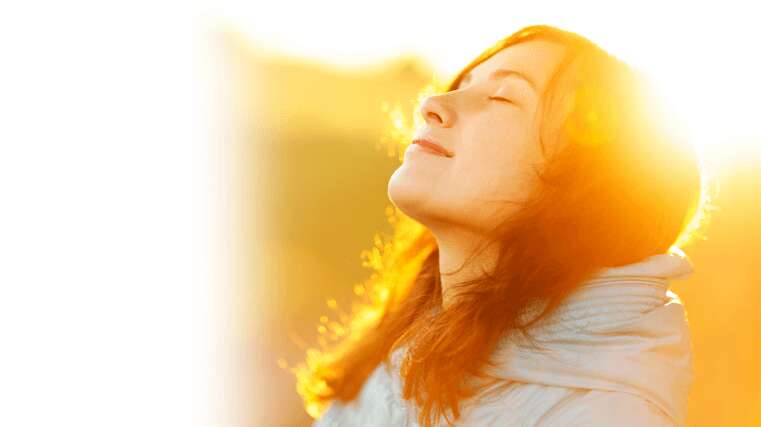 Woman bathed in sunlight, eyes closed, wind in her hair