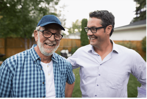 Elderly man, laughing, standing next to middle aged man smiling.