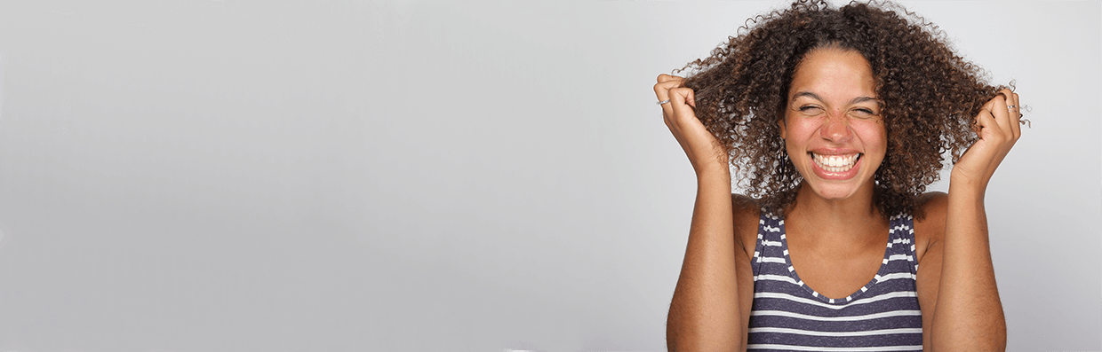 Woman smiling, holding her healthy hair, on a grey background. 