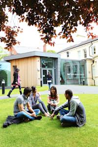 View of INTO Centre entrance with international group of students sat outside View of INTO Centre entrance with international group of students sat outside