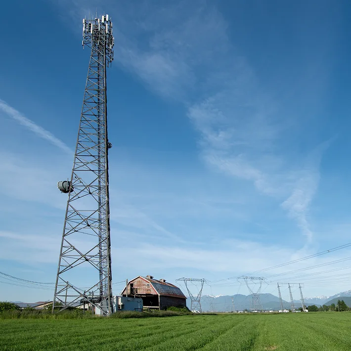 A tall cell tower located on a farm land nearby a barn.