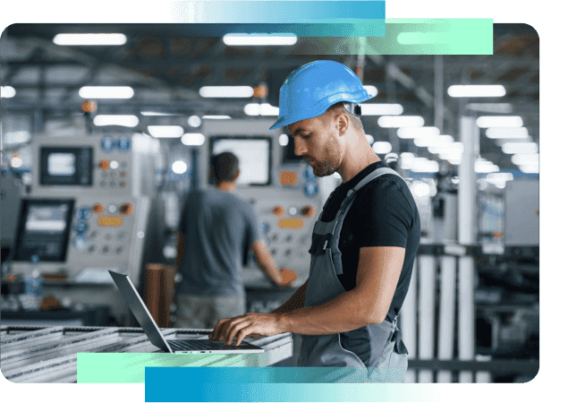 Man wearing a hardhat working on a laptop in a factory