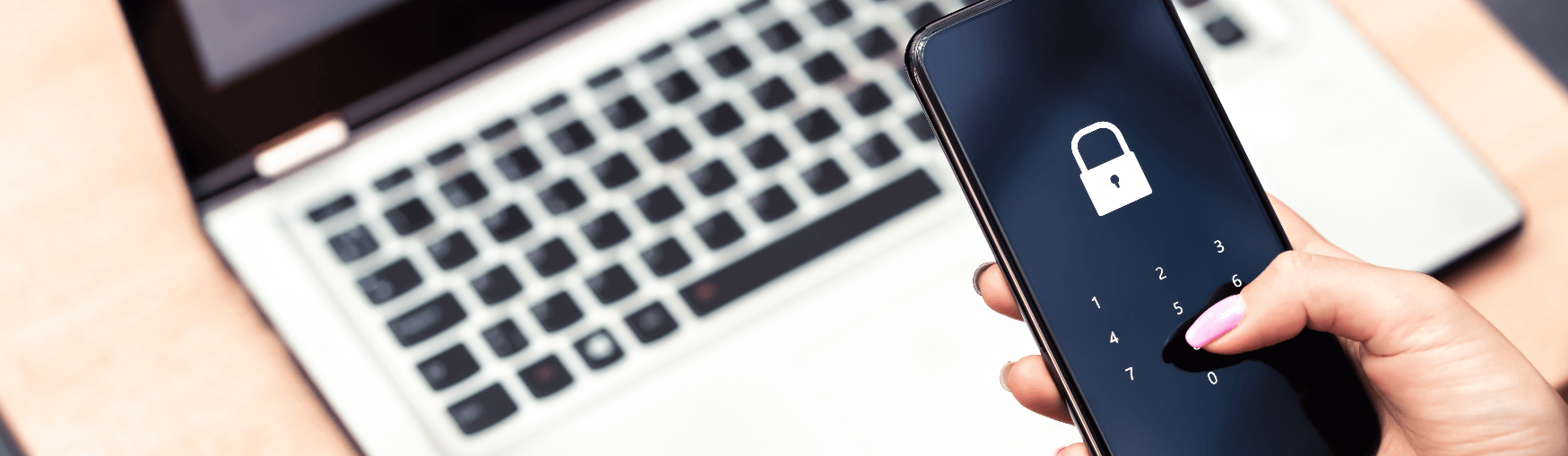 Hand holding a mobile phone locked to a passcode held over a laptop