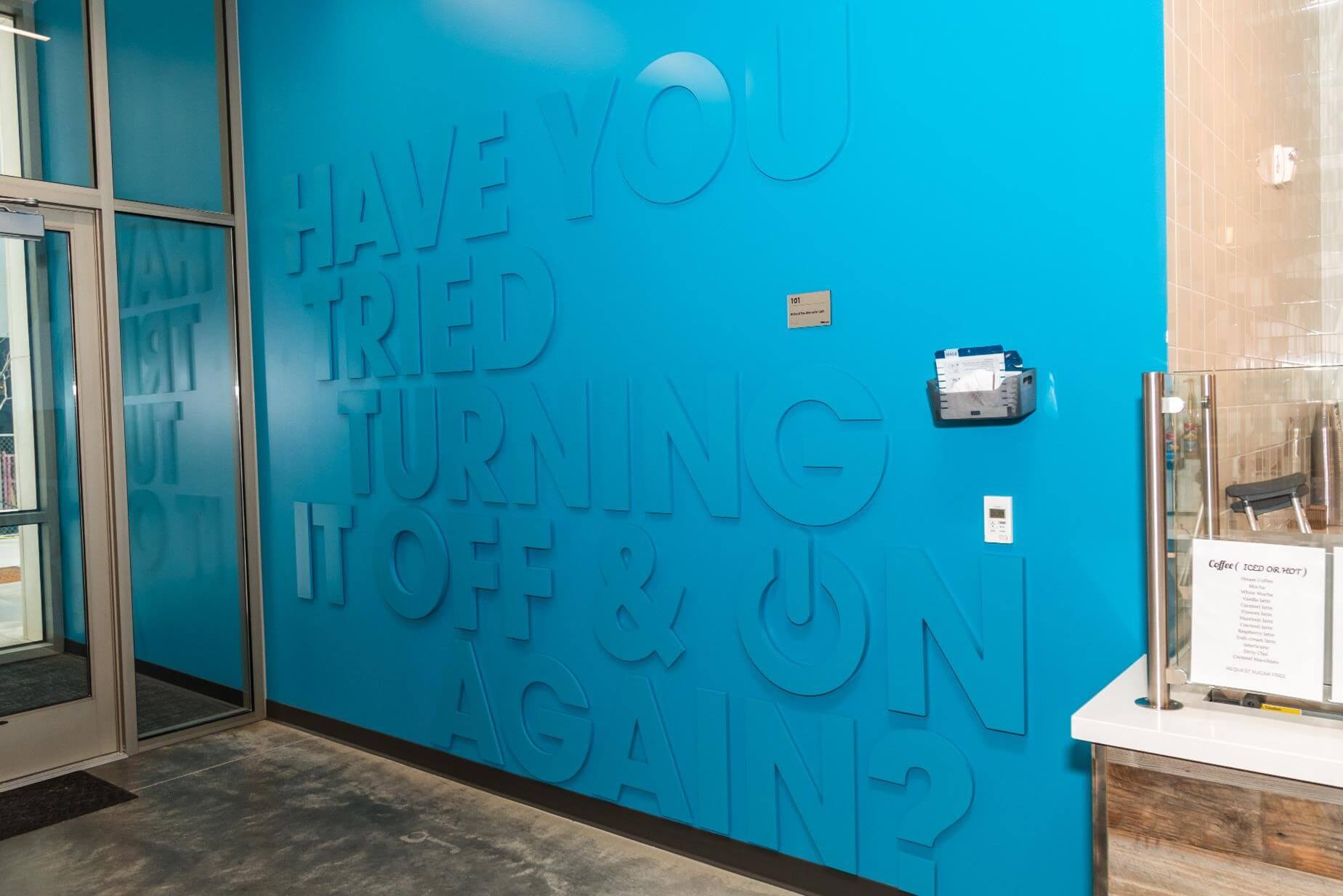 Wall of the PDQ cafeteria which has 'Have you tried turning it off and on again?' lettered on it in large, bold letters