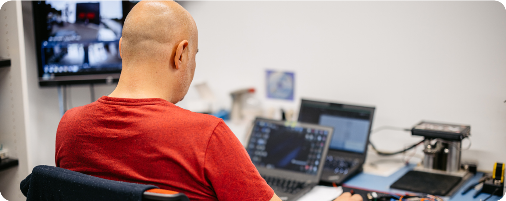 bald man with red shirt on two laptops