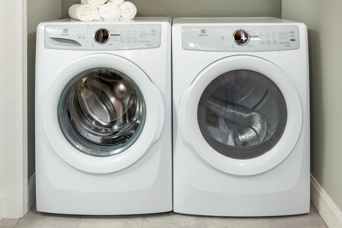 A close-up of a front-loaded white washer and dryer set with white towels rolled on top of the dryer.