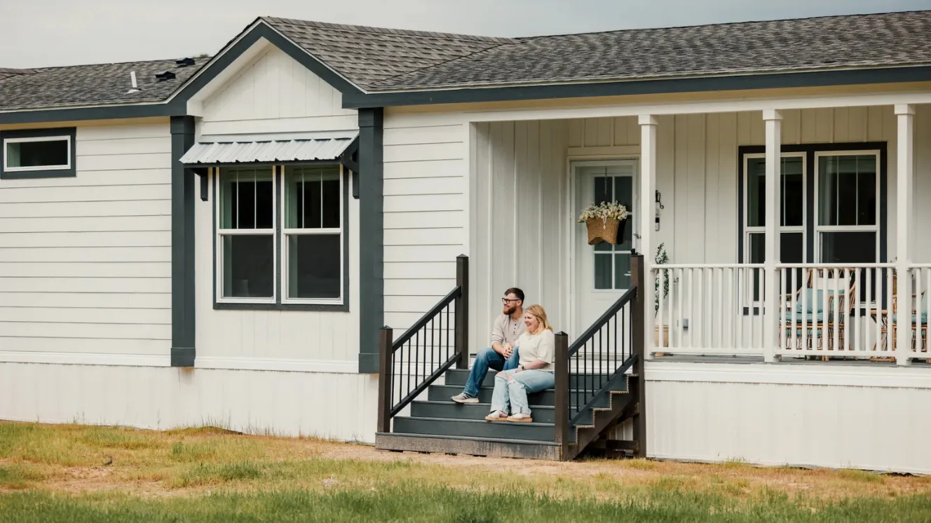 A couple sits on the steps of their front porch of a farmhouse manufactured home.