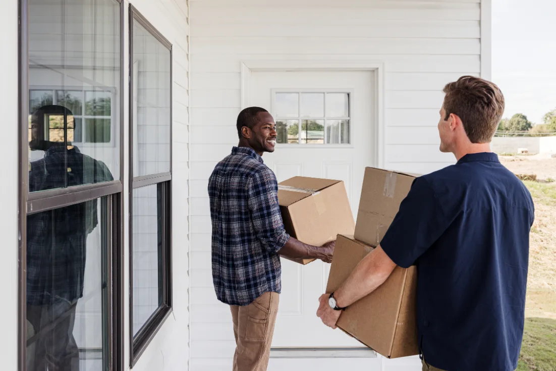 Two men carry moving boxes up to the front door of a home.