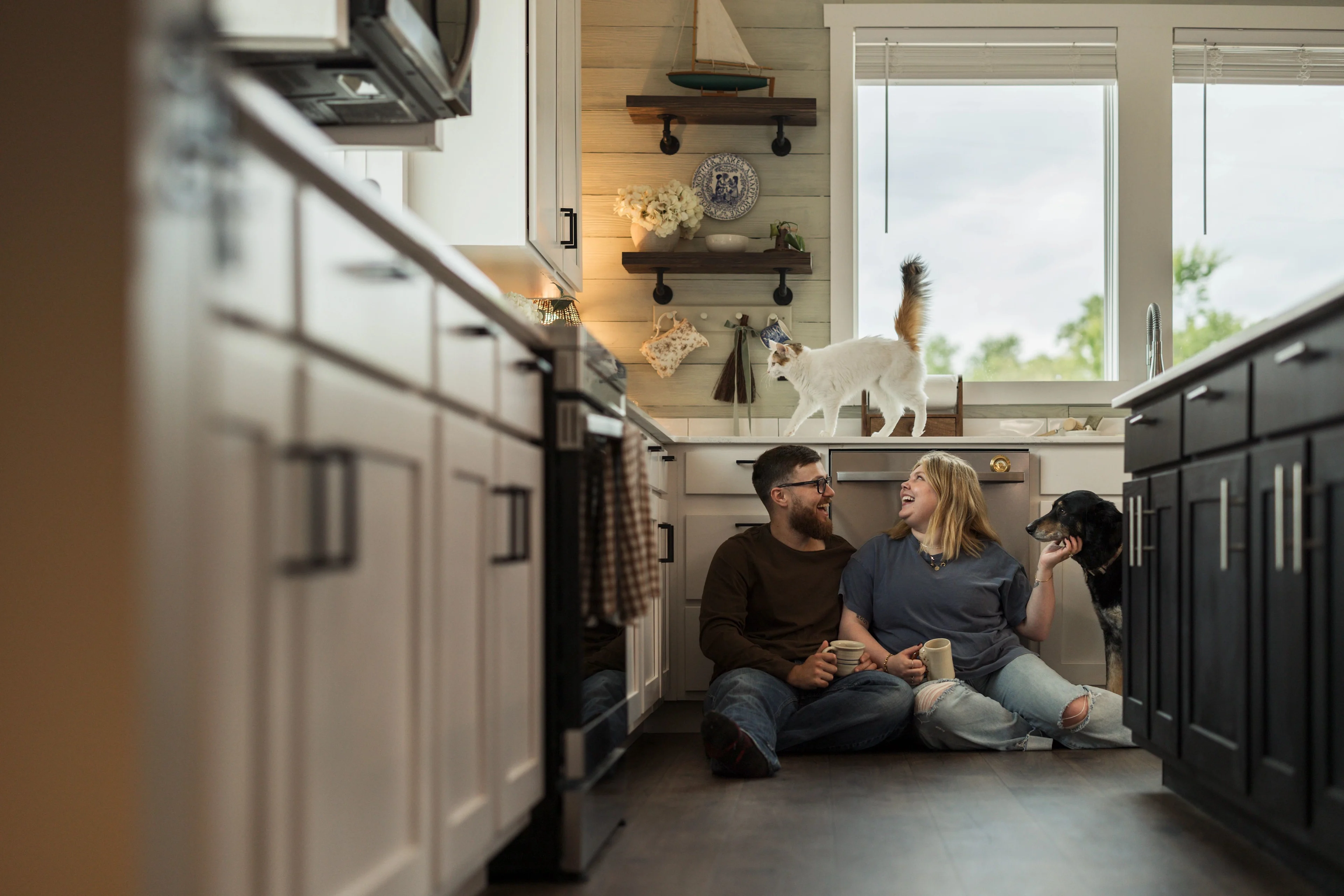 Koven and Josh Bruce drinking coffee and sitting on her kitchen floor with their dog and cat.