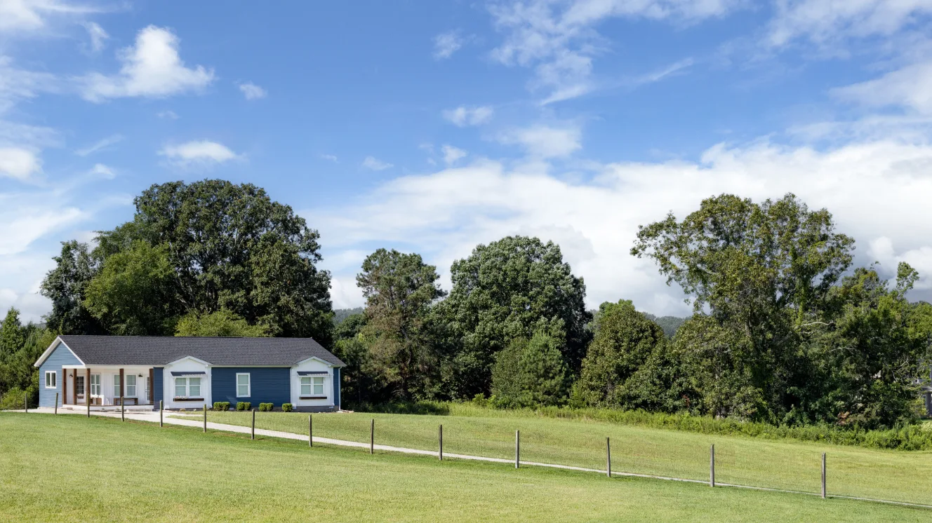 The blue and white exterior of a manufactured home down a long driveway.