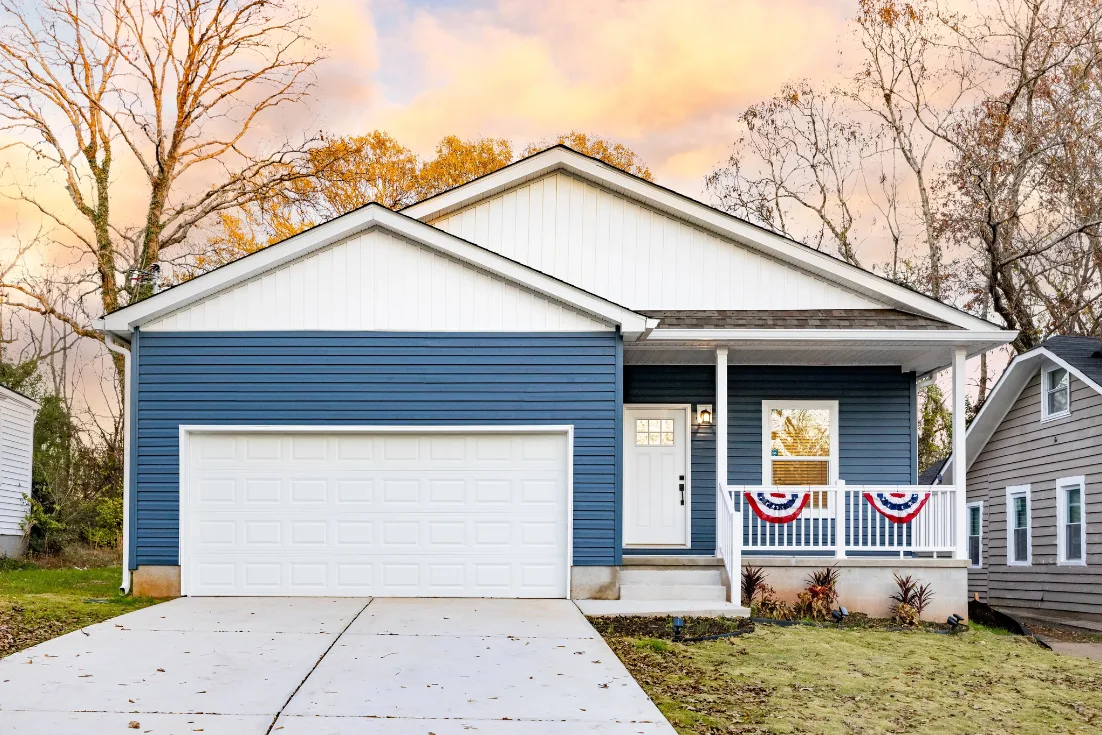 The exterior of a Clayton CrossMod home on a fall day that has blue siding , a white garage and front door and a front porch.