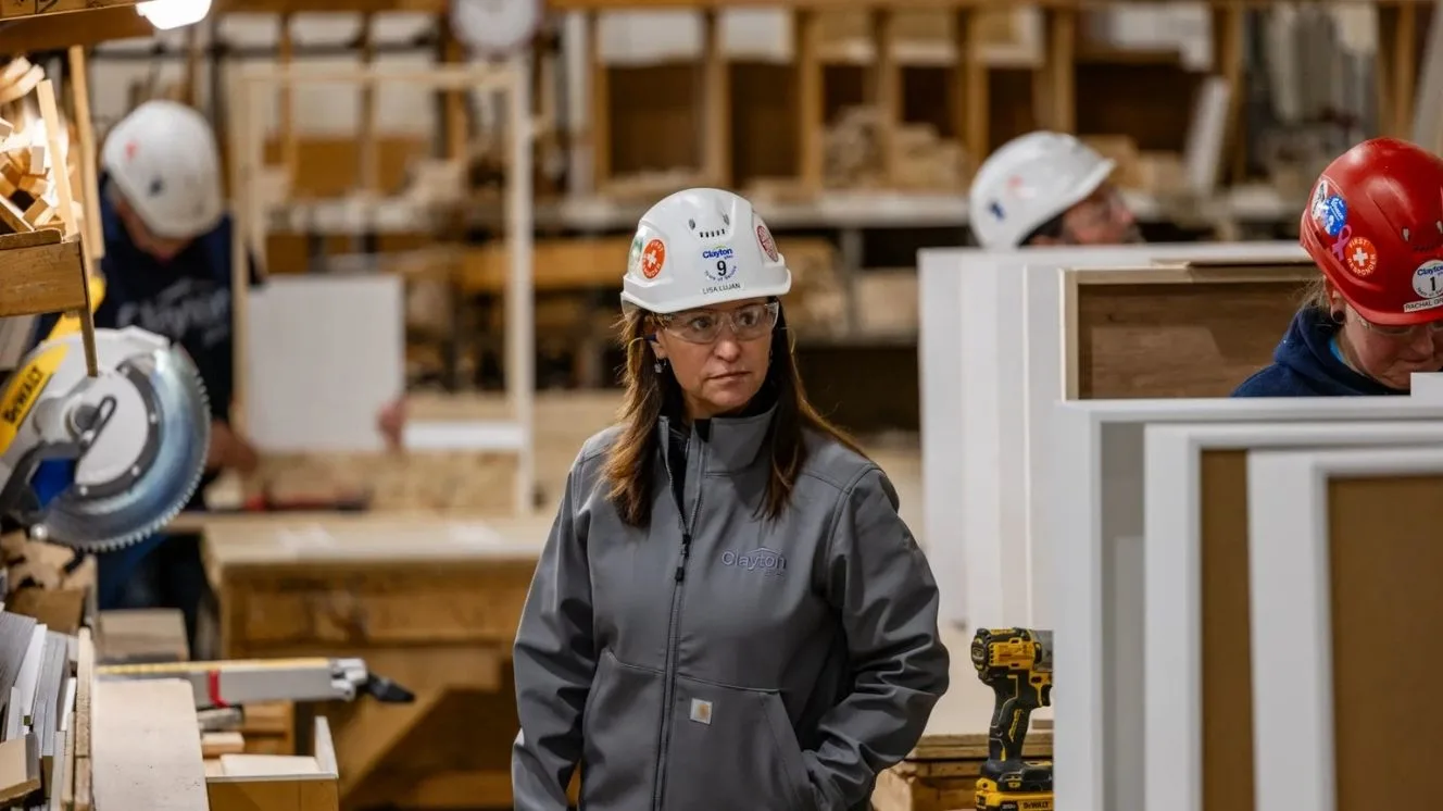 Lisa stands in a gray jacket and white hard hat inside a building facility.