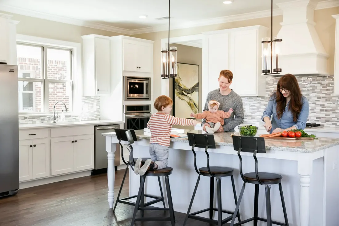 A family of four sit at a kitchen island while chopping vegetables in a new construction home.