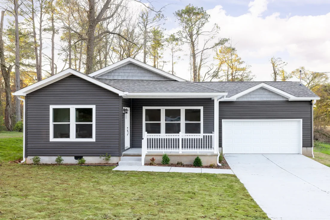The exterior of a Clayton CrossMod® home with gray siding, white trim and doors, a front porch, and an attached garage.